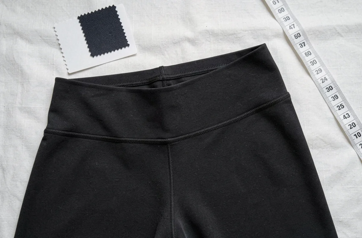 Détail en gros plan de la ceinture et du tissu d'un legging sculptant Leonie And Co noir en flat lay sur lin blanc